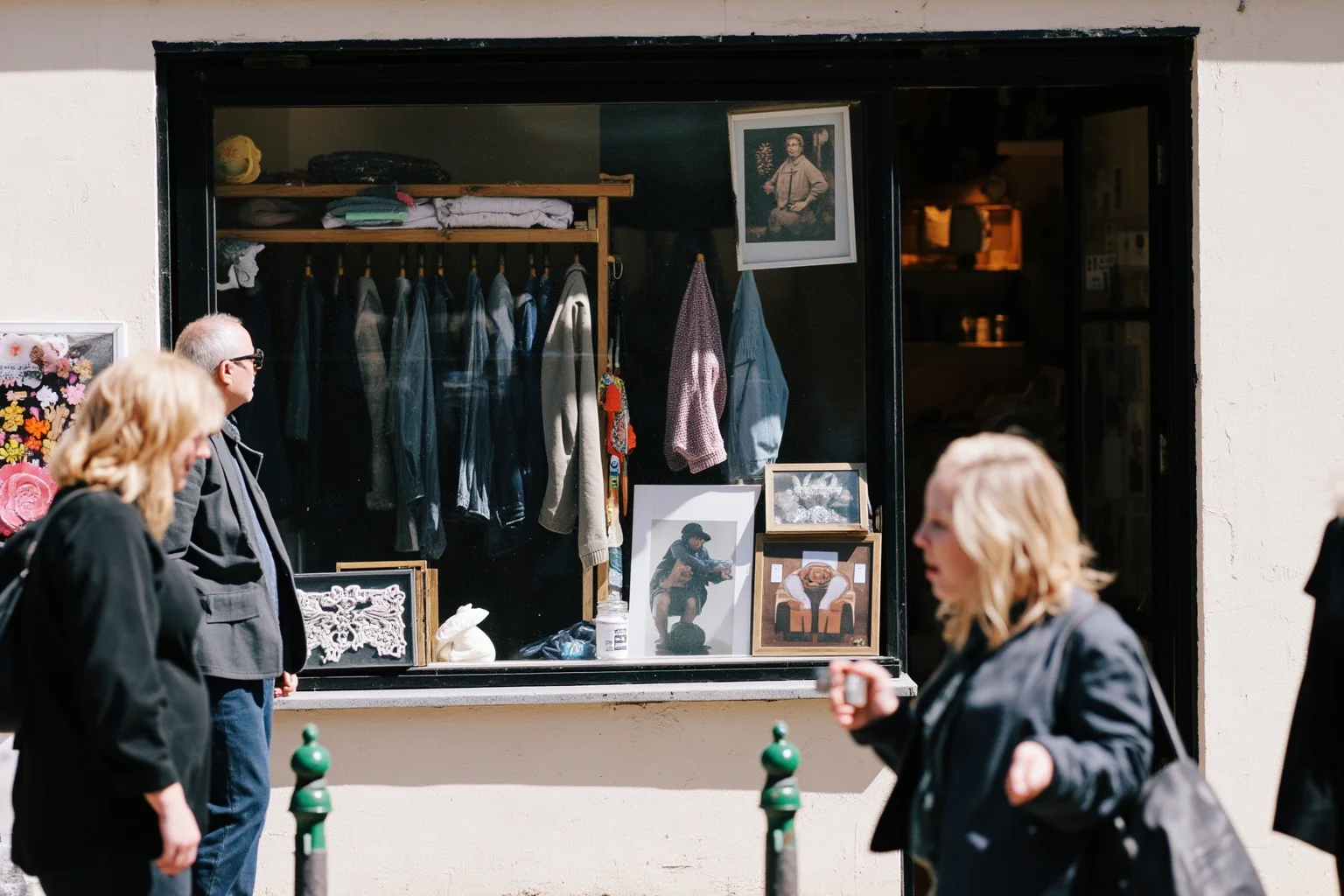 A secondhand shop window with used clothing and household items, with people browsing outside.