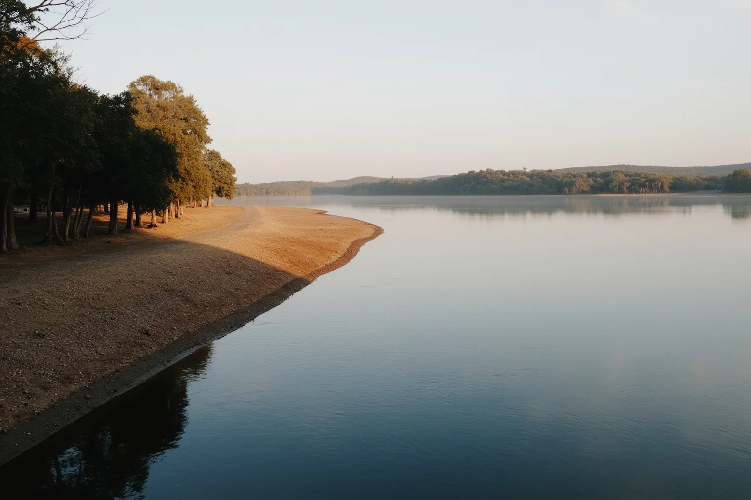 A serene morning view of a wide river with trees on the bank, empty shoreline, soft dawn light, no people.