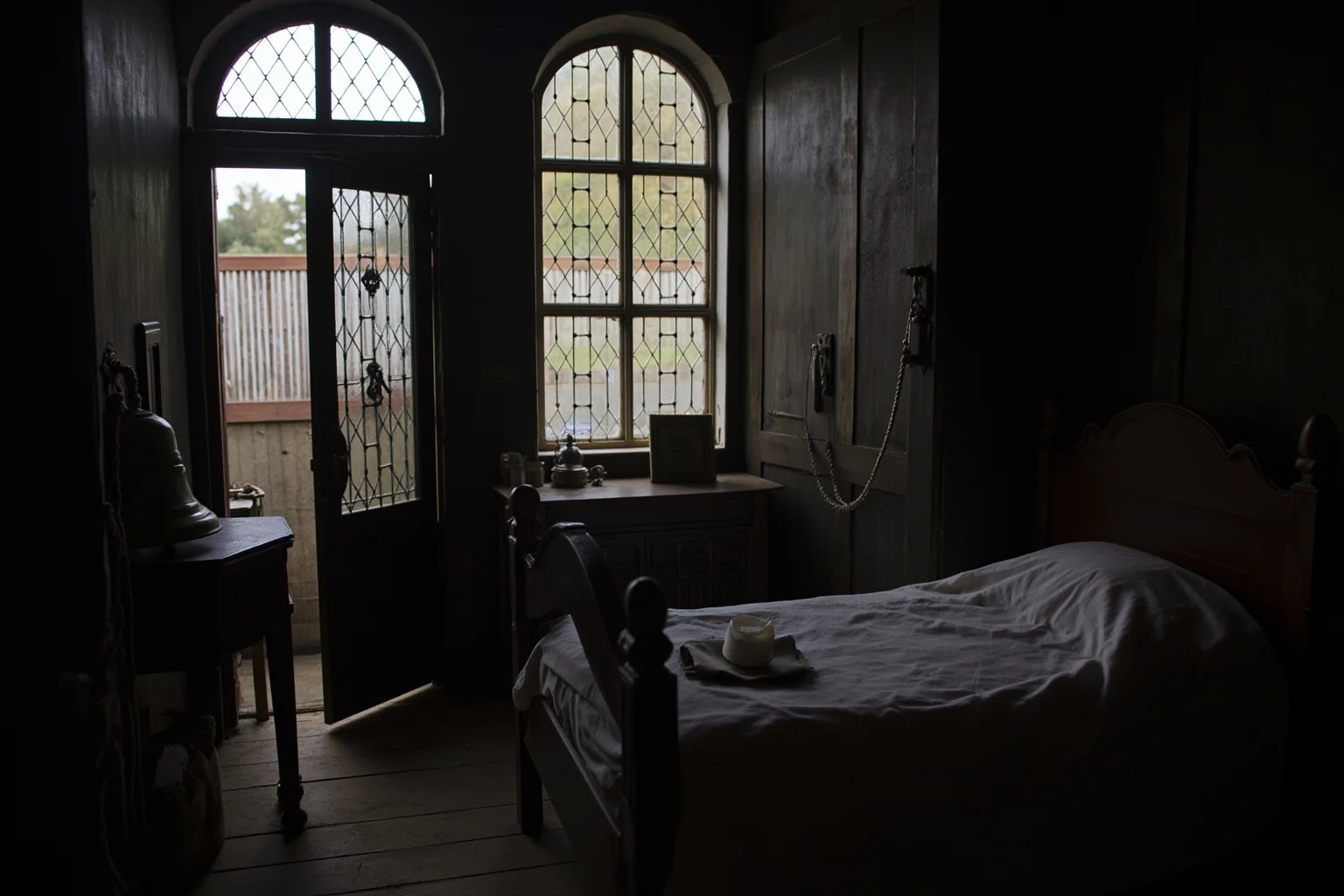 A sickroom in a seventeenth-century English house, a bell rope by the door, a Bible and candle on a side table, soft grey morning light through leaded windows.