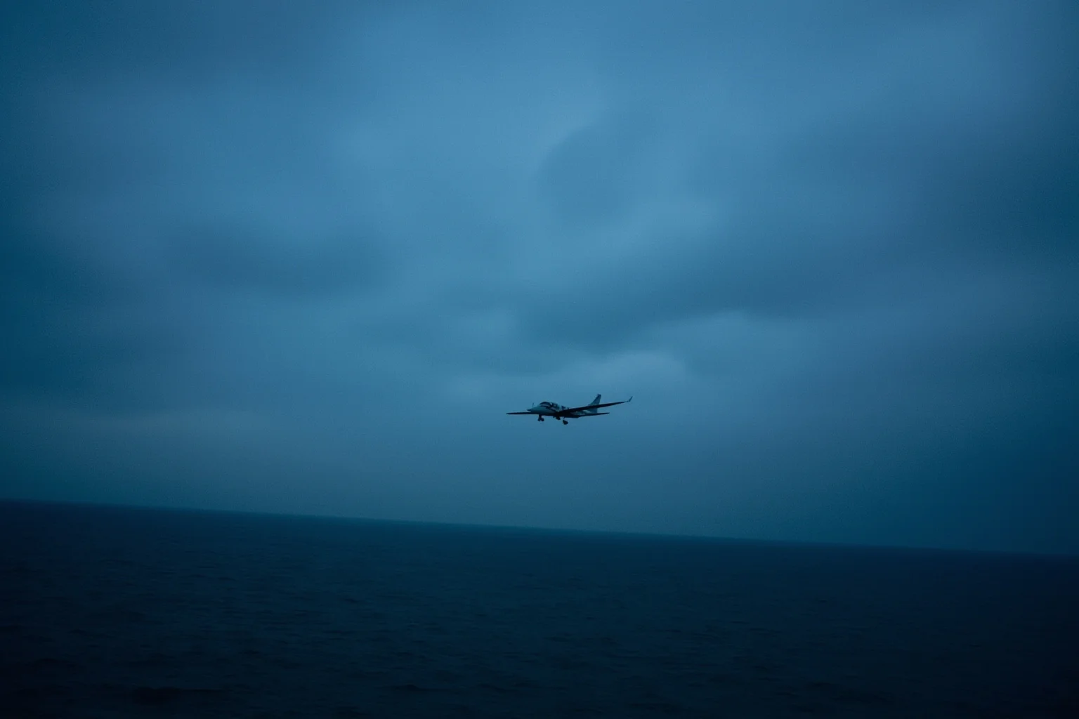 A small private plane flying over the Atlantic Ocean near Martha's Vineyard at dusk, moody blue and grey tones, no identifiable figures