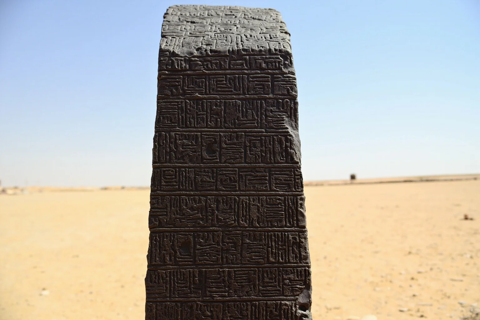Earliest Laws We Still Practice Today: 10 First Law Codes That Shaped Modern Rules 3 A tall dark stone stele covered in carved cuneiform script, standing in a desert setting under a clear sky, evoking the Code of Hammurabi.