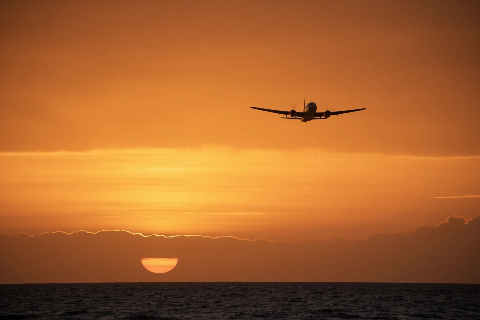 A vintage silver twin-engine aircraft silhouetted against a vast Pacific sunset sky above open ocean