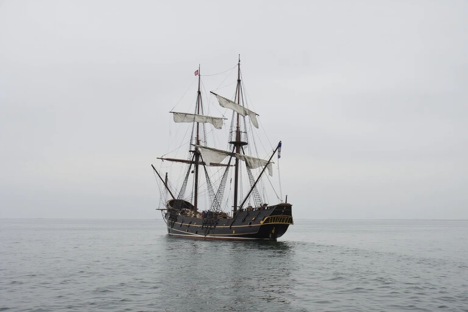 An empty 19th-century sailing brigantine drifting on calm grey ocean, sails partly furled, no crew visible on deck