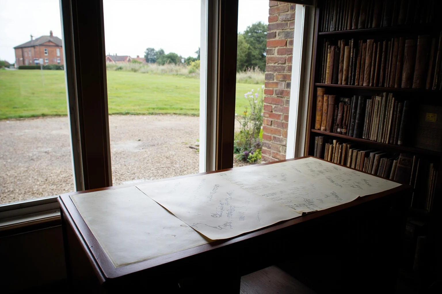 An English country house library with a mahogany desk, letter paper and a view of a gravel drive through tall windows, soft Regency daylight.