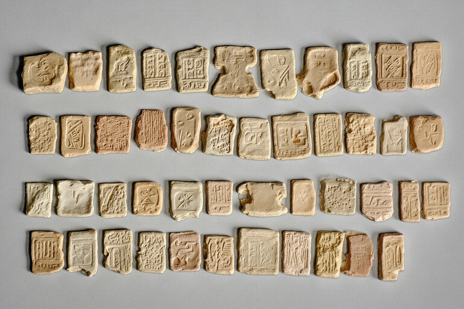 Ancient carved stone seals with short rows of undeciphered symbols arranged on a neutral surface, archaeological catalog style