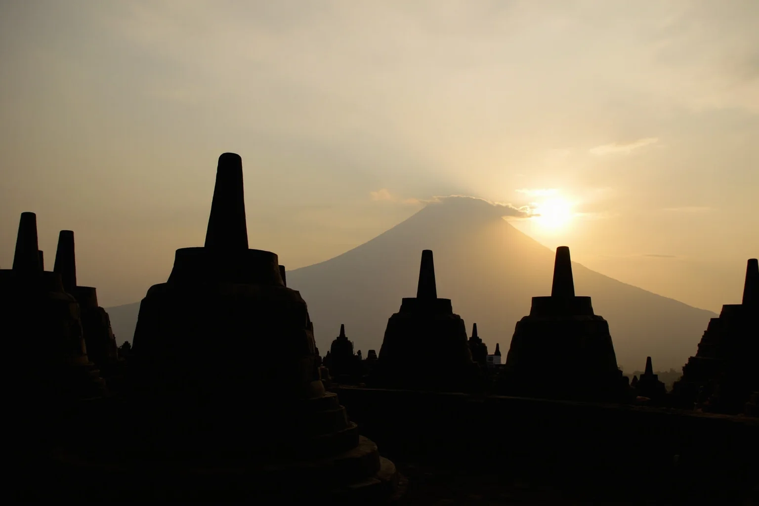 Borobudur's stone stupas and seated Buddha statues silhouetted against a volcanic horizon at sunrise