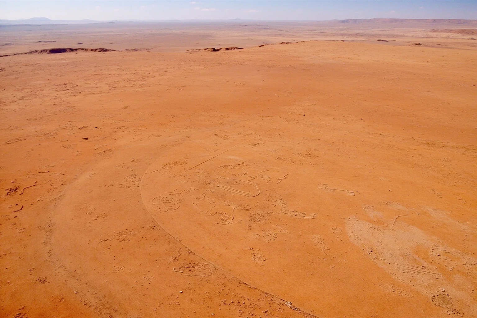 Desert plateau in Peru with enormous geometric lines and animal-shaped geoglyphs carved into the dry earth, aerial view