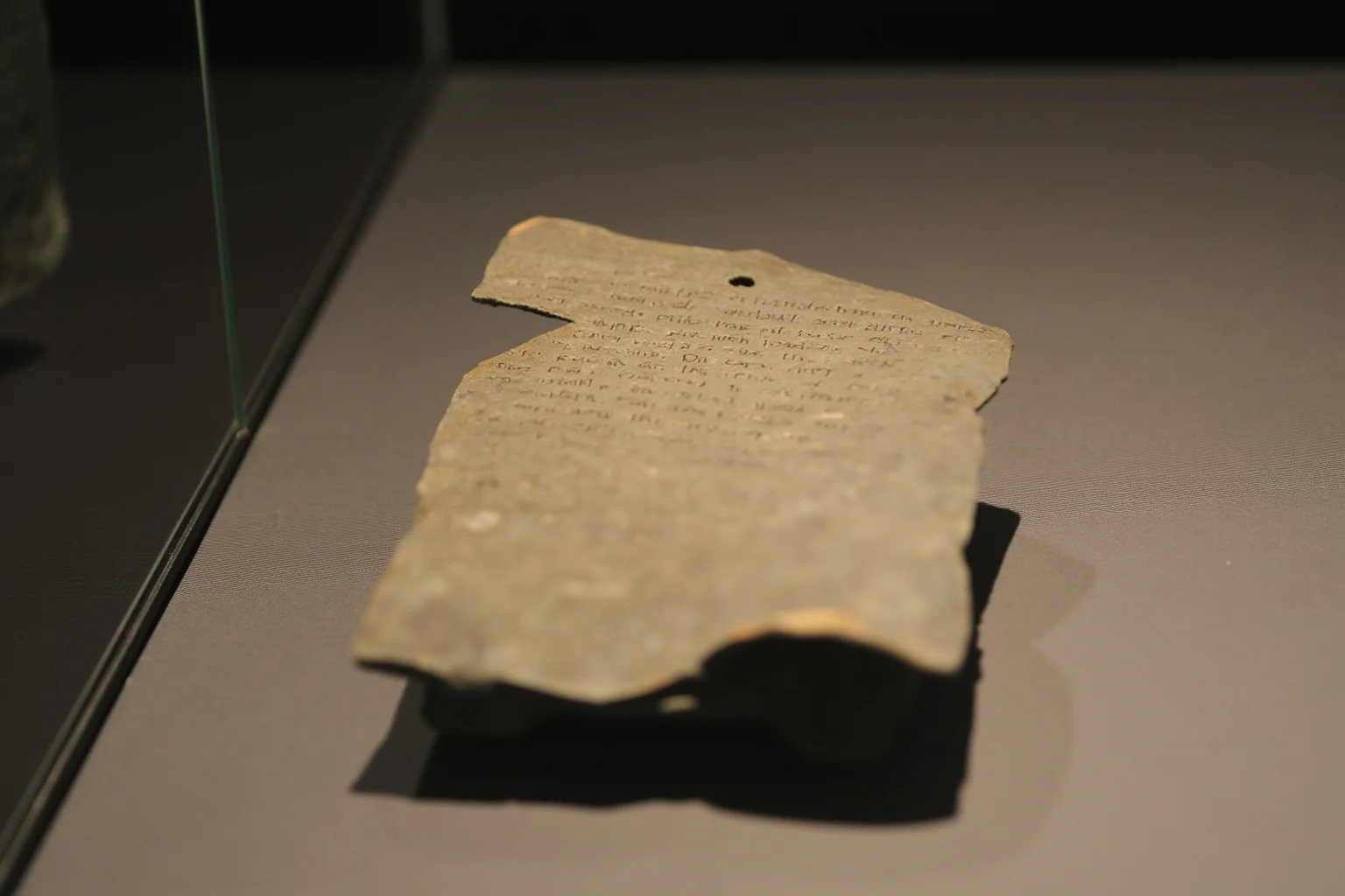 23 Ancient Graffiti Messages That Sound Shockingly Modern 13 Folded lead curse tablet with inscribed Latin text and a pierced hole, museum display case, soft focused lighting, no people.