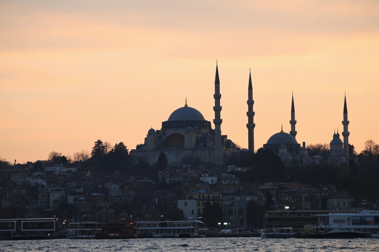 Hagia Sophia's dome and minarets seen across Istanbul at dusk, warm sky and calm water