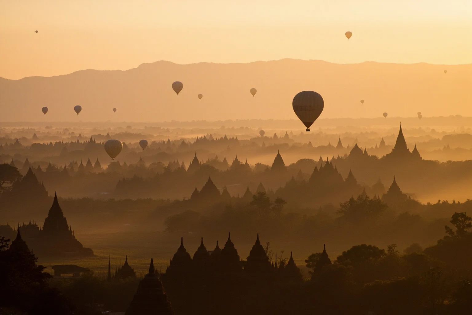 Hot-air balloons drifting over the temple plain of Bagan at dawn, brick stupas scattered across the landscape