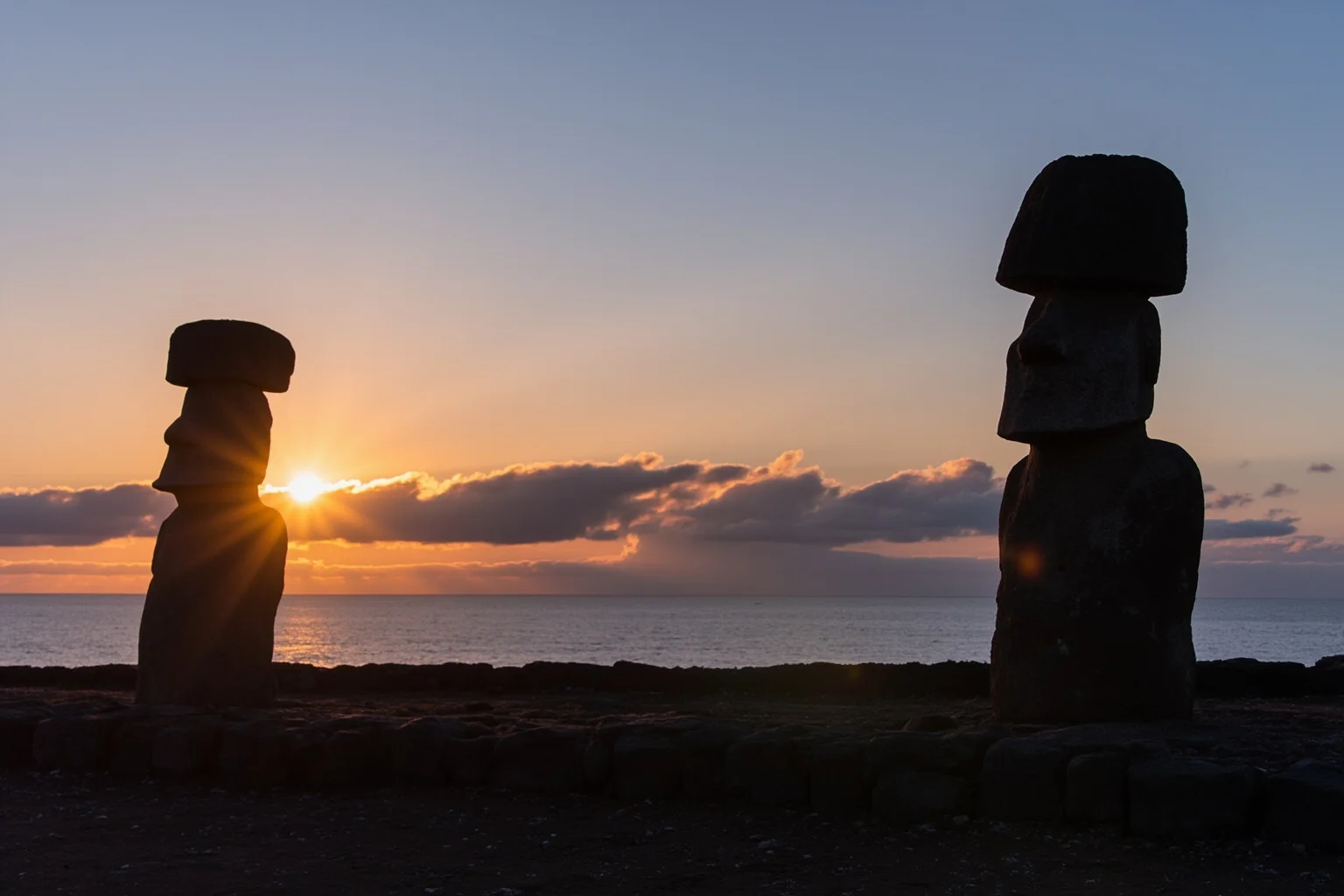 Moai statues of Rapa Nui standing on an ahu platform against a Pacific sunset