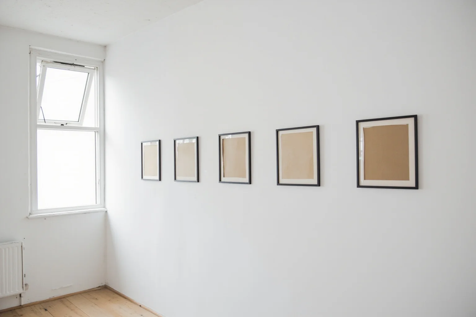 Modern art museum gallery with five empty frames on a white wall, a sash window left open, morning light, clean minimalist composition.