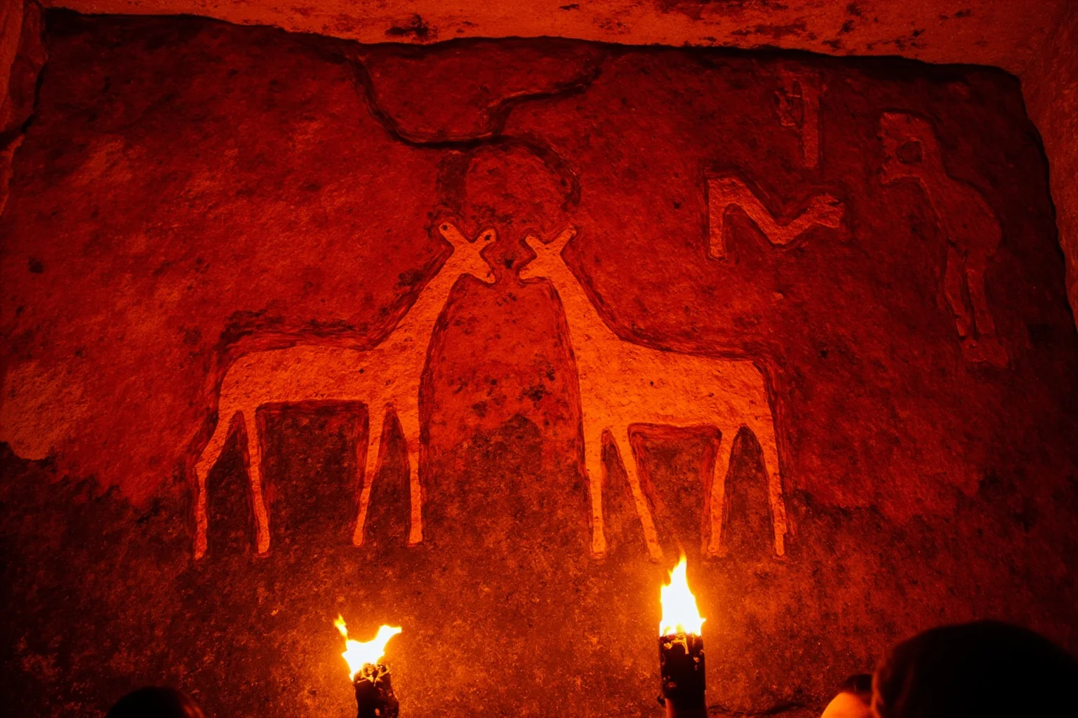 24 Facts About Prehistoric Humans 12 Prehistoric cave wall painting of animals in red and ochre pigments, lit by flickering torchlight.
