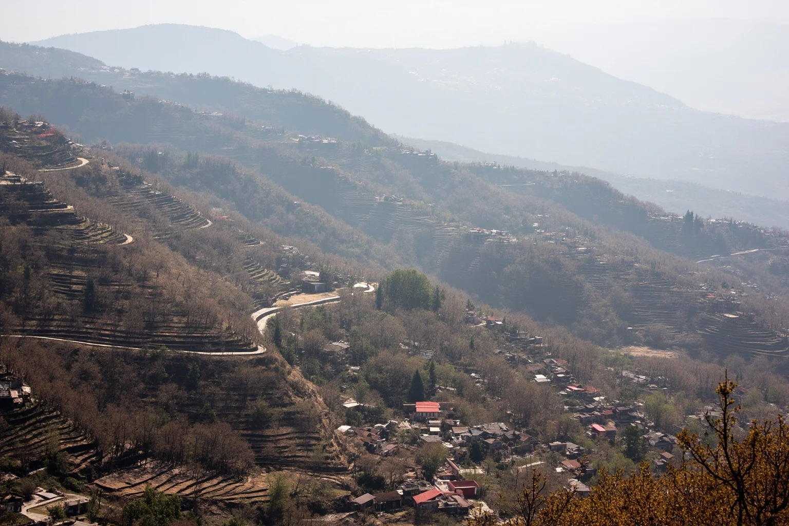 Rural mountain village with terraced fields and distant marching columns, 20th-century historical atmosphere