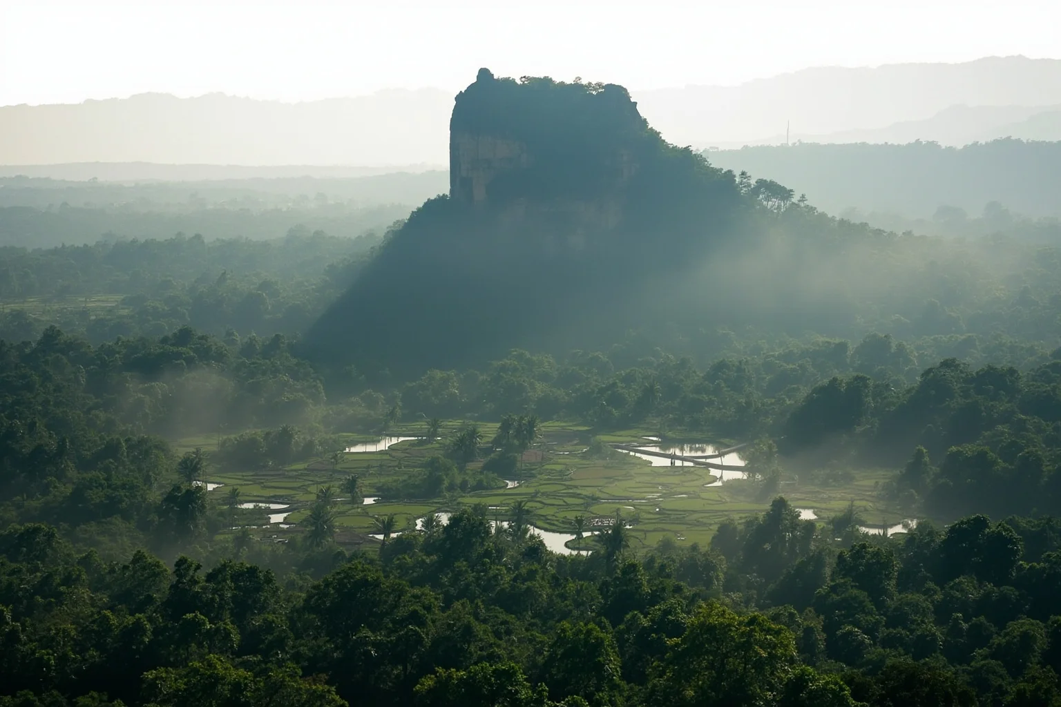 Sigiriya rock fortress rising above jungle and symmetrical water gardens in Sri Lanka, morning mist