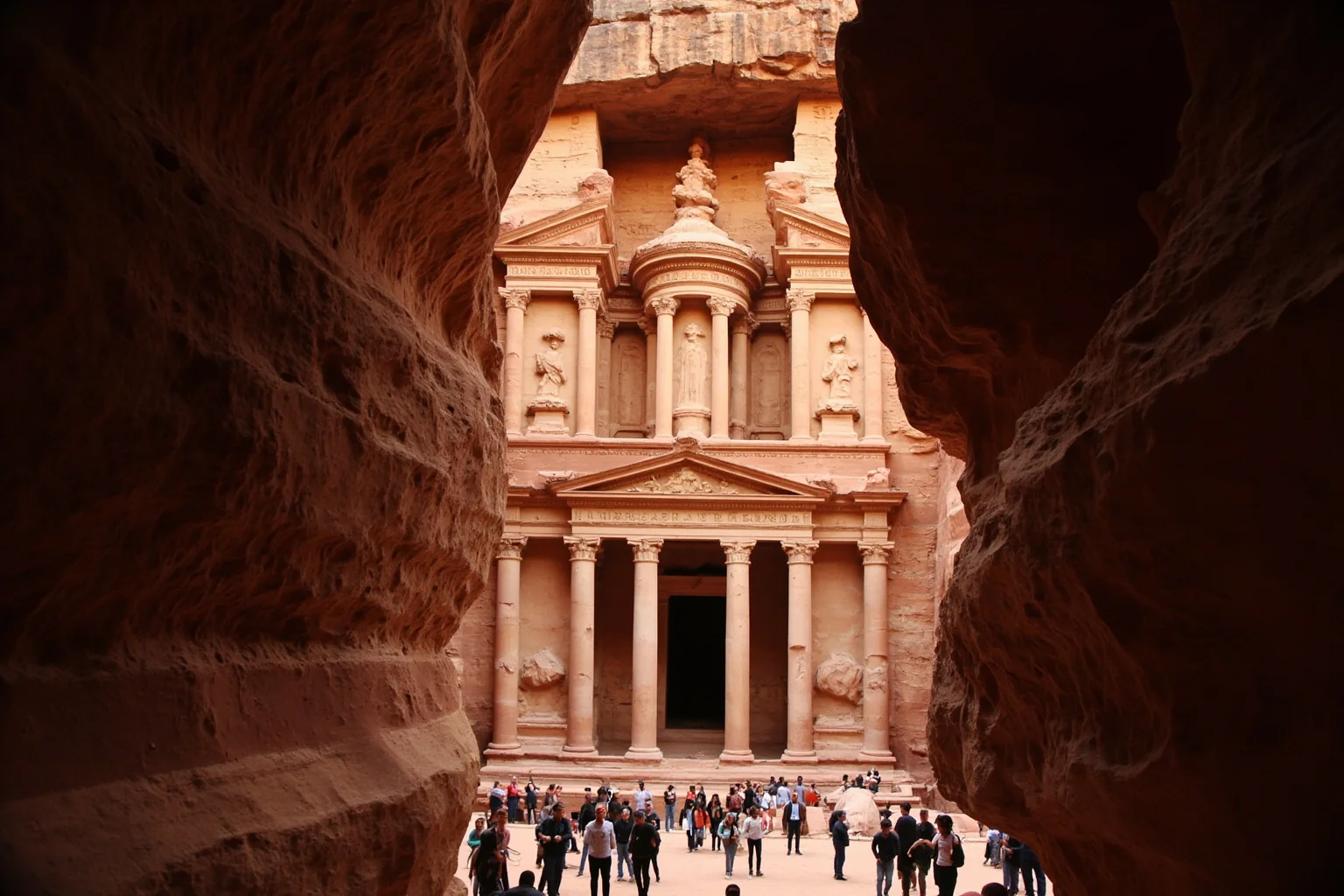 The Al-Khazneh facade at Petra carved into rose-colored sandstone, viewed through the narrow Siq gorge
