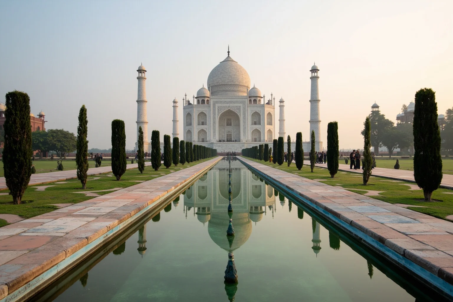 The Taj Mahal reflected in the long water channel at dawn, white marble and cypress trees framing the view